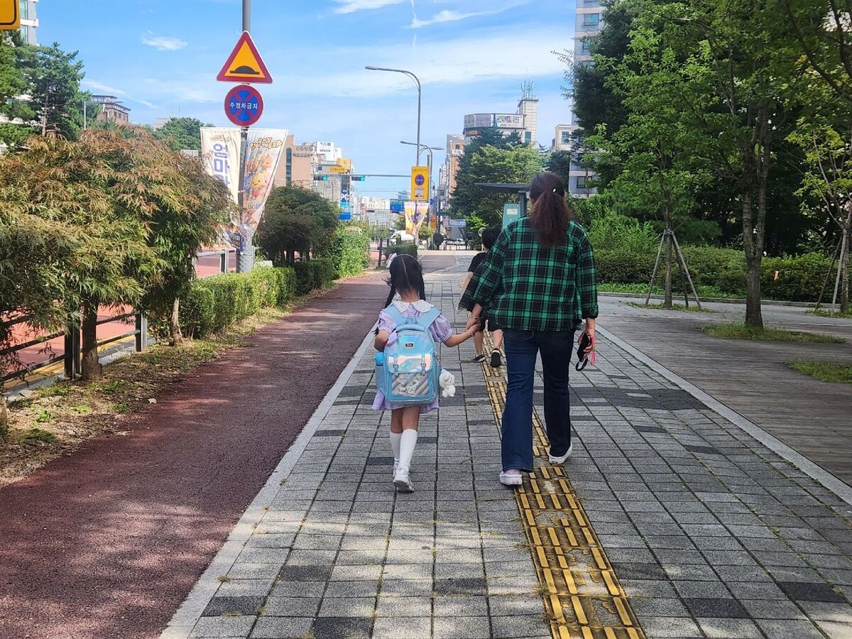 수원새빛돌봄의 새빛돌보미가 초등학교 저학년 학생의 등하교에 동행하고 있다. 보호자가 갑작스러운 사정으로 등하교를 돕기 어려울 때 통장·지역사회보장협의체 위원 등이 돌보미로 나서는 서비스다. 2025년 7월 10개 동에서 시범 운영한 뒤 같은 해 11월 44개 모든 동으로 확대됐다. 수원시 제공